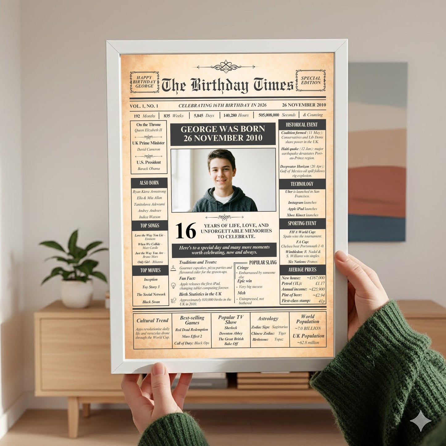 A person is holding up a framed newspaper-style birthday announcement for a young man named George, celebrating his 16th birthday.